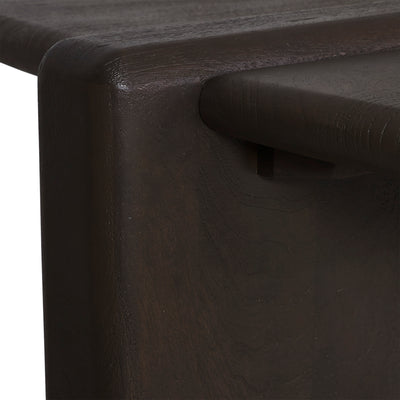 Close-up detail of a dark brown wooden furniture piece, showing the corner joint and a round wooden pull handle on a dark wood surface.