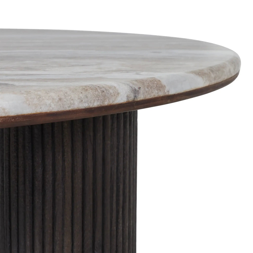 Close-up of a round dining table showing a light gray and white marbled stone top with a dark brown wood edge, supported by a dark brown fluted pedestal base, on a white background.